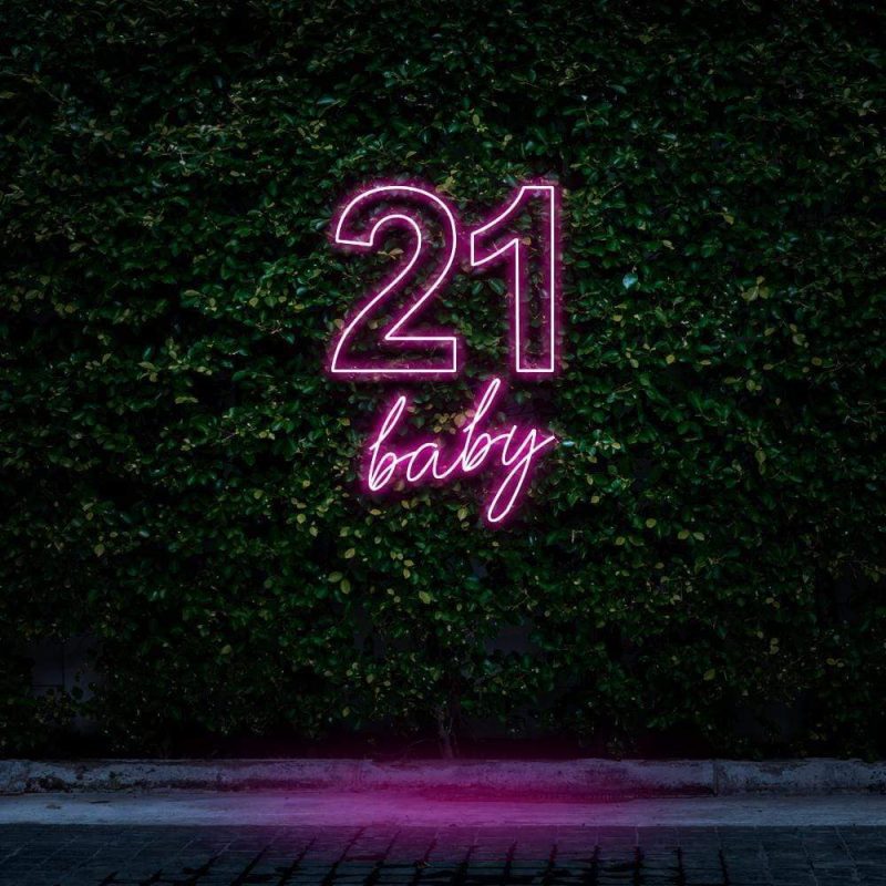 Bright pink neon sign displaying "21 Baby," glowing against a green leafy background, perfect for 21st birthday celebrations and trendy party decorations.