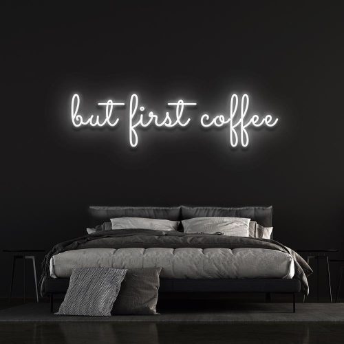 Cold white "But First Coffee" LED neon sign displayed above a sophisticated bed setup with a dark wall background, ideal for minimalist coffee enthusiasts.